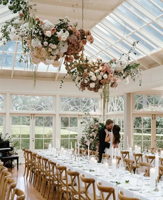Couple embrace under floral installation in the conservatory