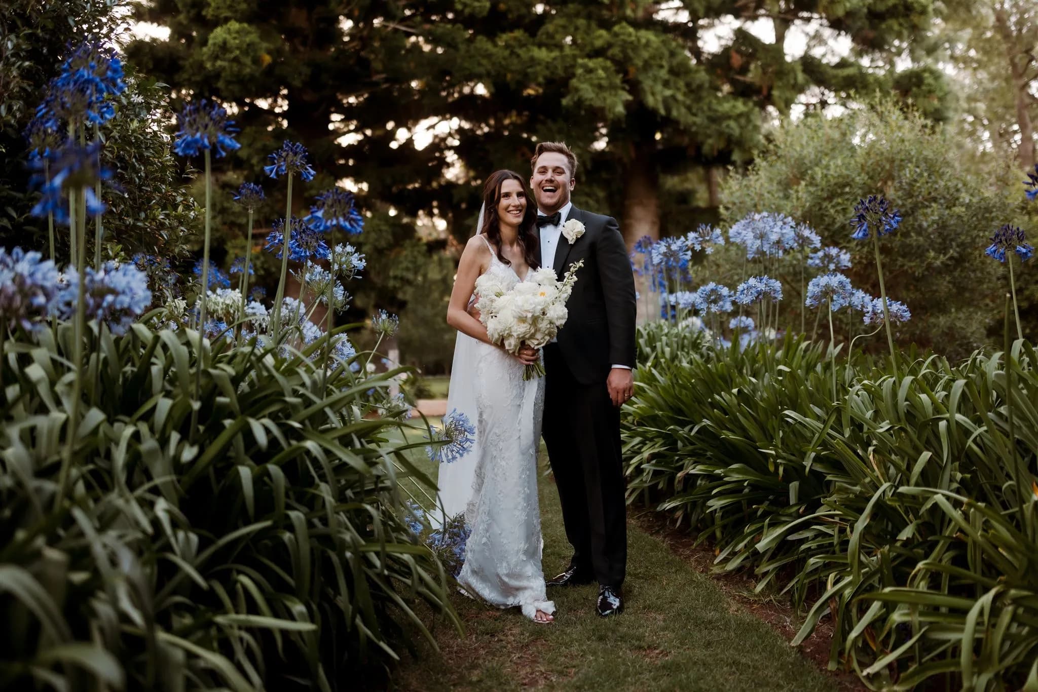 Bride and groom stading in garden with purple flowers