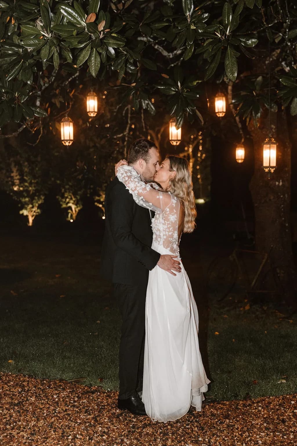 Bride and groom kissing under lantens in tree outside