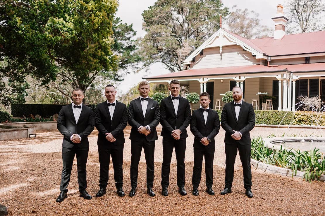 Groom and groomsman standing in front of homestead