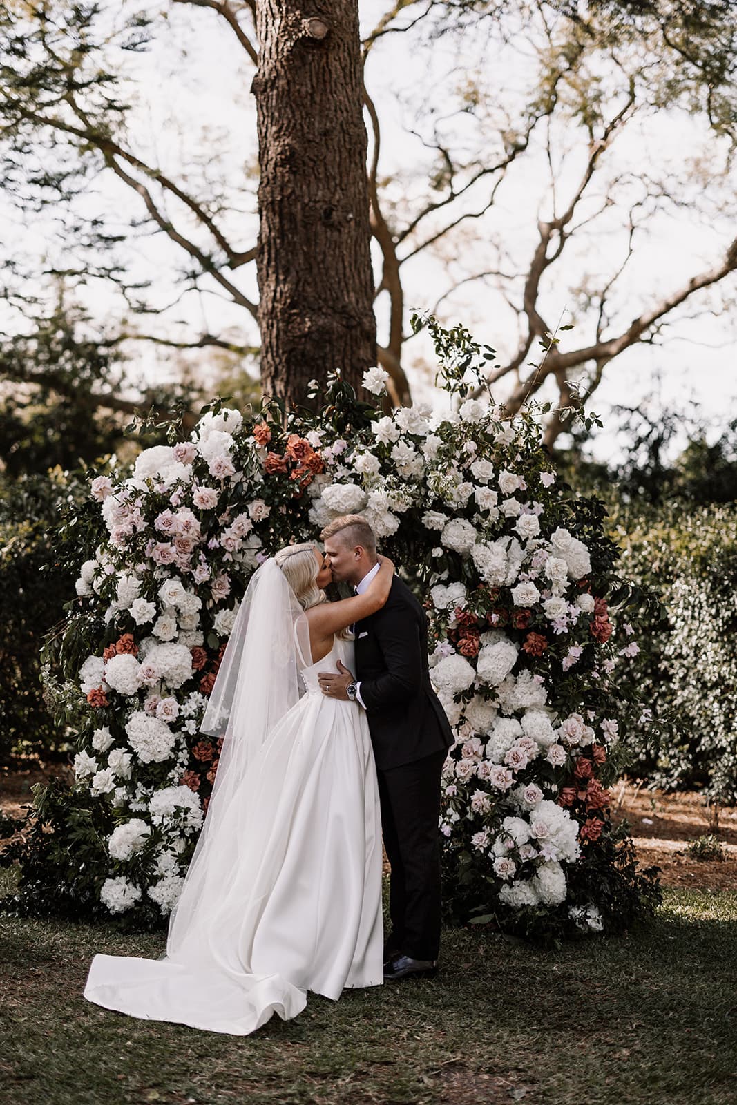 Bride and groom kissing in front of tree