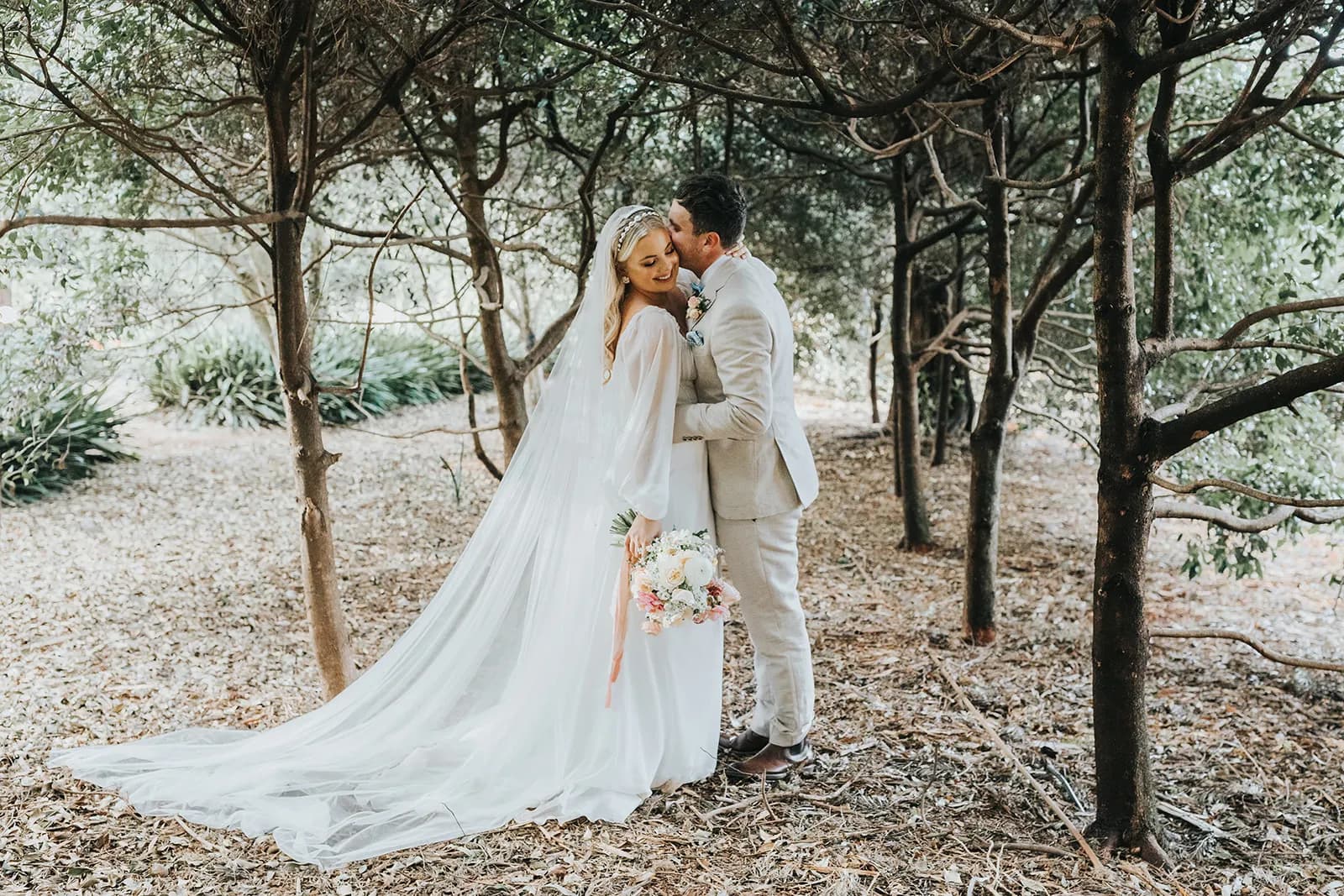 Bride and groom kissing under trees