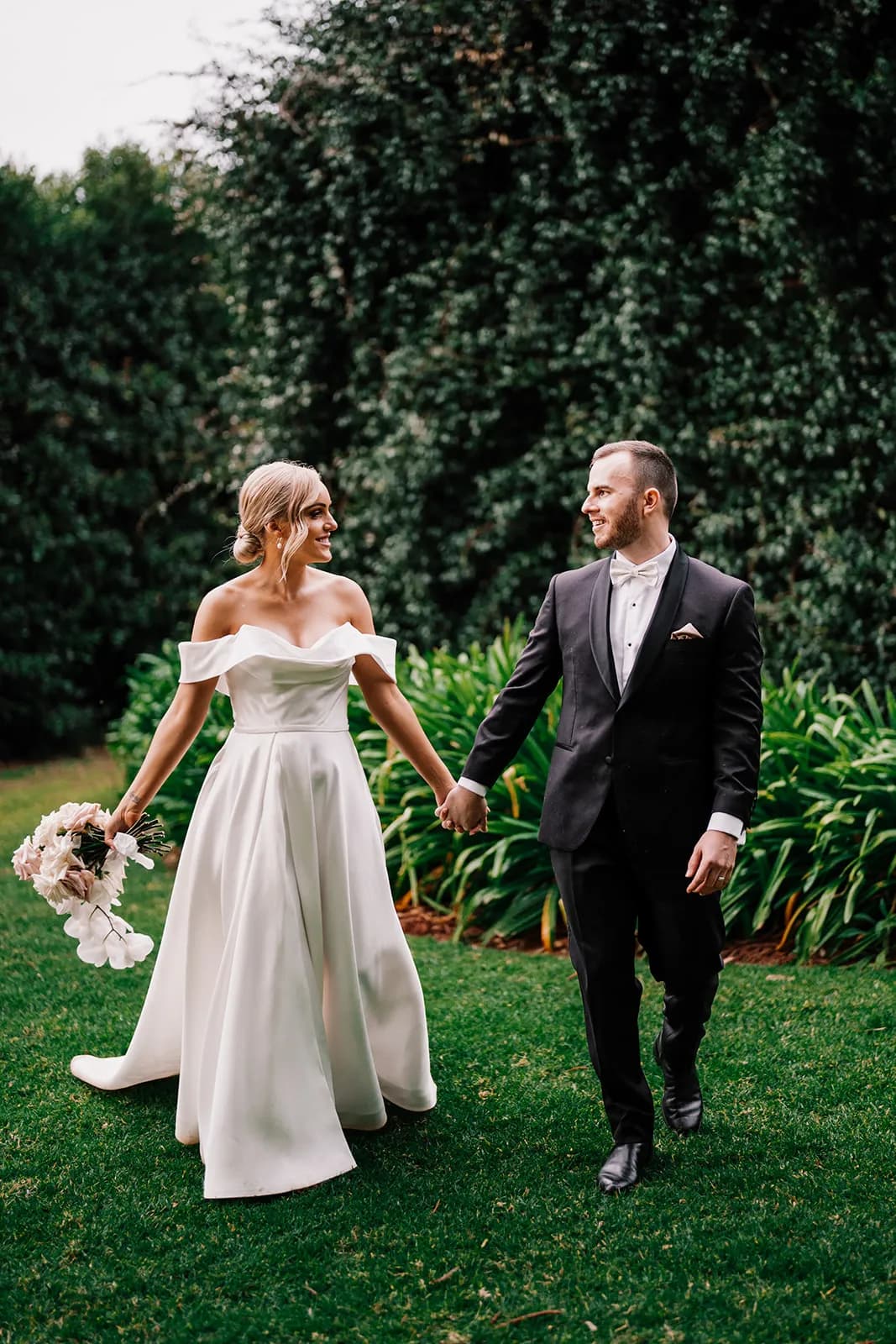 Bride and groom walking through the gardens holding hands