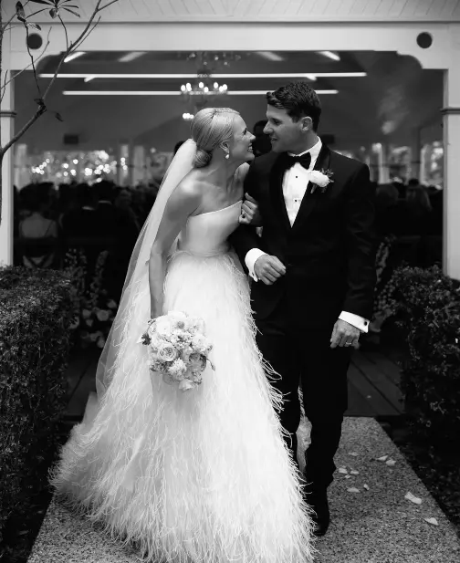 A just-married bride and groom walking out of the wedding venue with their arms linked