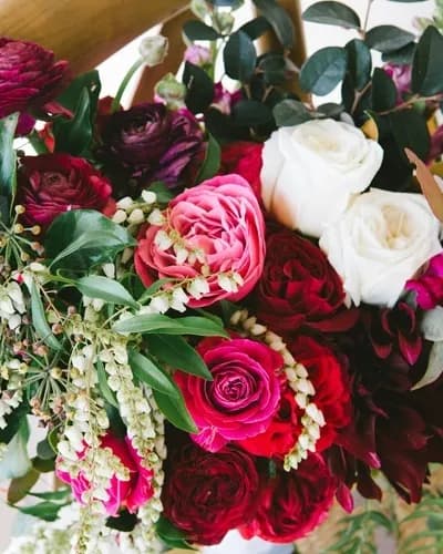 A vibrant bouquet of assorted flowers, including pink, red, and white roses, along with sprigs of white blooms and greenery. The bouquet is full and lush, showcasing a mix of colors and textures.